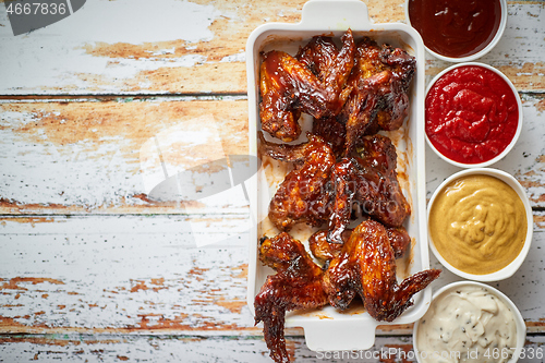 Image of Chicken wings in thick barbecue sauce with various side dips. Served on white cast iron dish