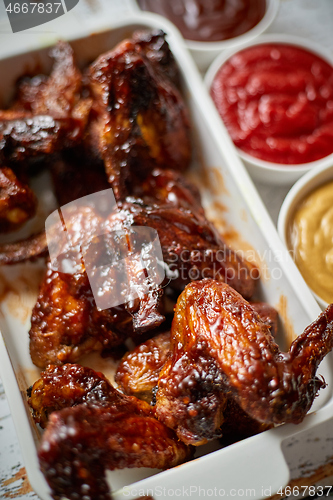 Image of Chicken wings in thick barbecue sauce with various side dips. Served on white cast iron dish