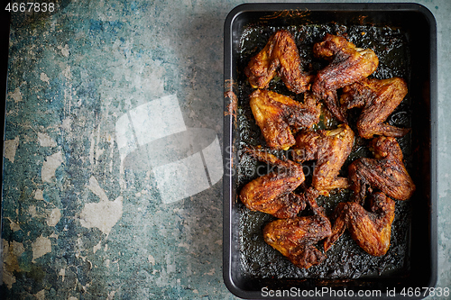 Image of Grilled chicken wings in spices in black metal baking tray on stone table. Top view