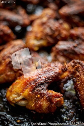 Image of Grilled chicken wings in spices in black metal baking tray on stone table. Top view