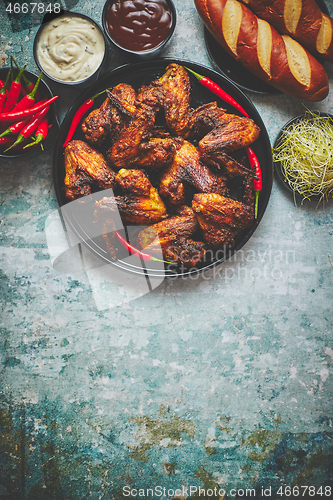 Image of Grilled chicken wings with chilli pepper on a rustic plate served with various dips and bread