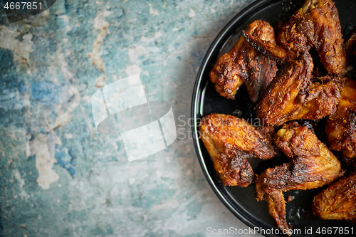 Image of Grilled chicken wings on a black ceramic plate. Placed on a stone