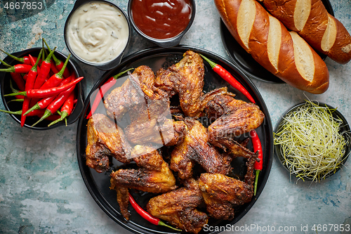 Image of Grilled chicken wings with chilli pepper on a rustic plate served with various dips and bread