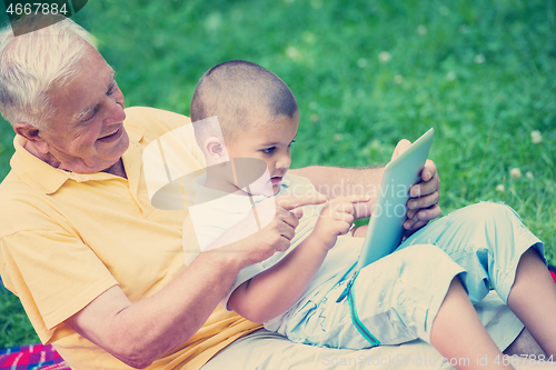 Image of grandfather and child in park using tablet