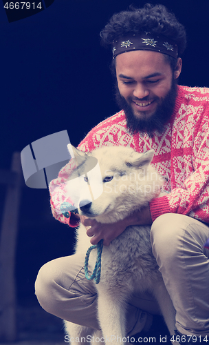 Image of young man playing with dog in front of wooden house