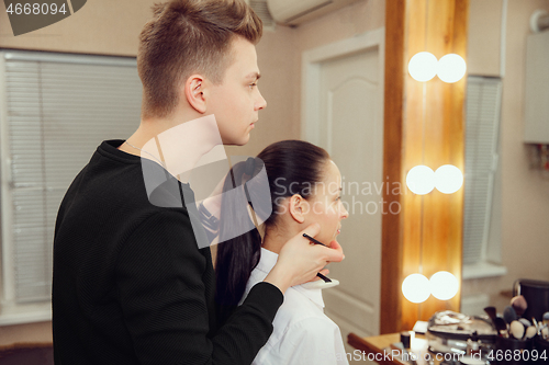 Image of Professional makeup artist working with beautiful young woman