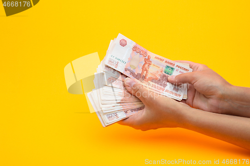 Image of In hands lies a bundle of five thousandth bills on a yellow background