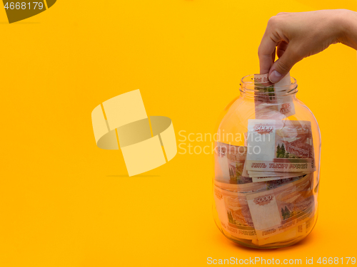 Image of Hand stuffs a five thousandth bill into a glass jar