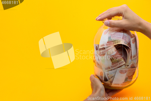 Image of Hands holding a three-liter jar in which lie five thousandth bills