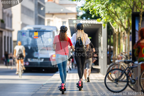 Image of Rear view of trendy fashinable teenager girls riding public rental electric scooters in urban city environment. New eco-friendly modern public city transport in Ljubljana, Slovenia