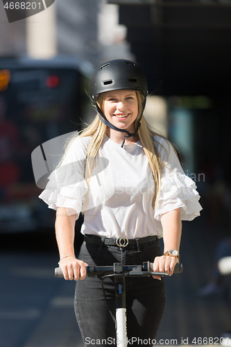 Image of Trendy fashinable teenager, beautiful blonde girl riding public rental electric scooter in urban city environment. Eco-friendly modern public city transport