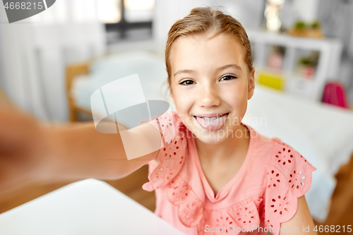 Image of girl taking selfie and showing tongue at home