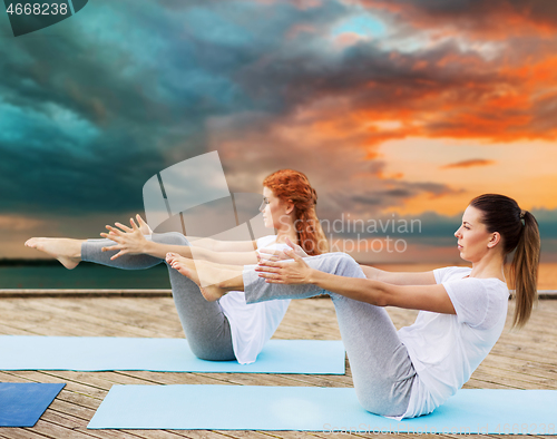 Image of women making yoga in half-boat pose outdoors