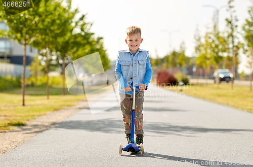 Image of happy little boy riding scooter in city