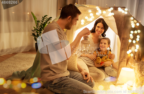 Image of happy family playing in kids tent at night at home