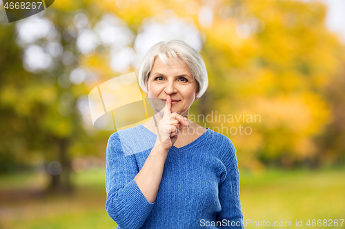 Image of senior woman making shush gesture in autumn park