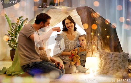 Image of happy family playing in kids tent at night at home