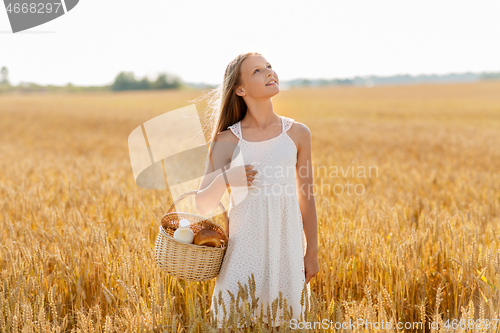 Image of girl with bread and milk in basket on cereal field