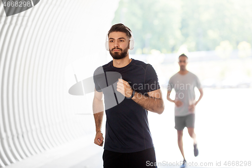 Image of male friends with headphones running outdoors