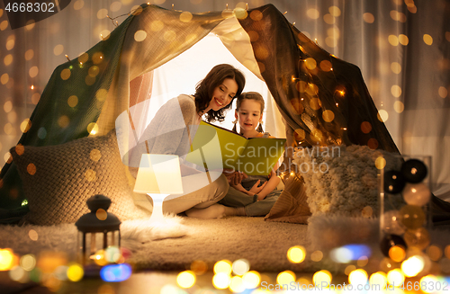 Image of happy family reading book in kids tent at home