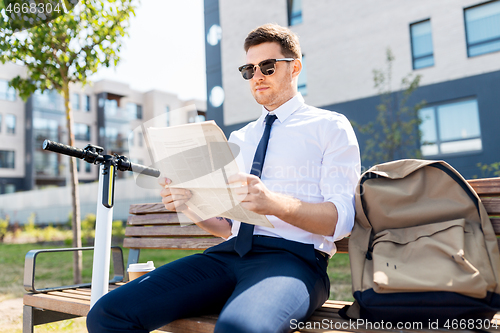 Image of businessman with scooter reading newspaper in city