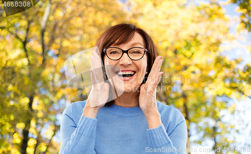 Image of senior woman in glasses calling over autumn park