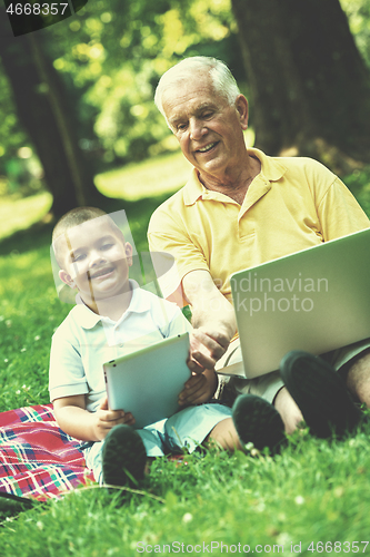 Image of grandfather and child in park using tablet