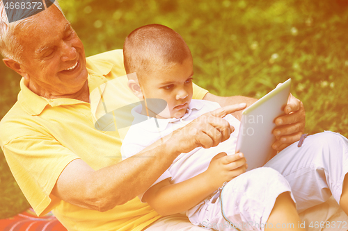 Image of grandfather and child in park using tablet