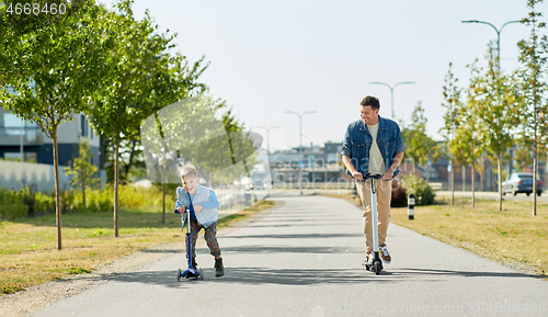 Image of father and little son riding scooters in city