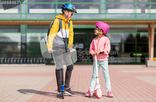 Image of happy school children in helmets riding scooters