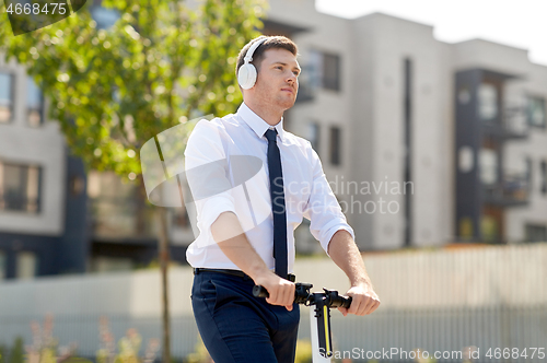 Image of businessman with headphones riding scooter in city
