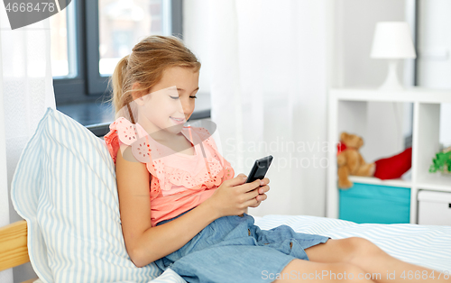 Image of girl using smartphone sitting on bed at home