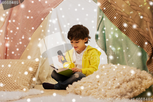 Image of happy boy reading book in kids tent at home