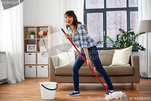 Image of happy asian woman with mop cleaning floor at home