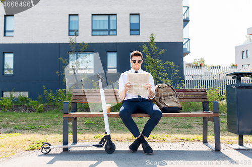 Image of businessman with scooter reading newspaper in city