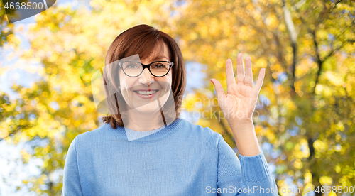 Image of portrait of senior woman in glasses waving hand