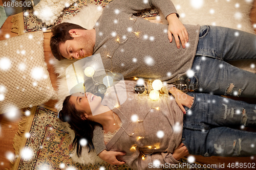 Image of happy couple with garland lying on floor at home