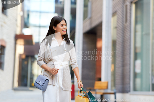 Image of asian woman with shopping bags walking in city