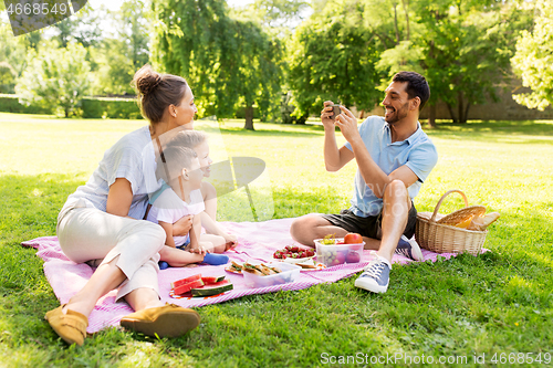 Image of father taking picture of family on picnic at park