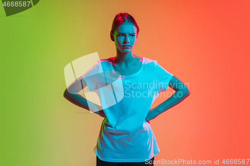 Image of Young caucasian girl\'s portrait on gradient green-orange studio background in neon light