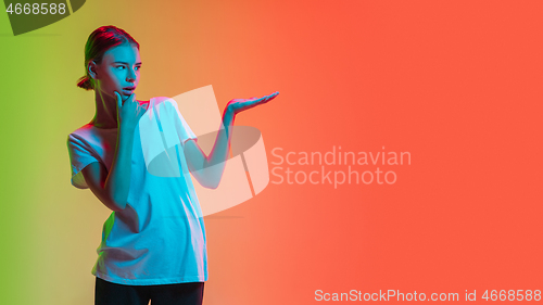 Image of Young caucasian girl\'s portrait on gradient green-orange studio background in neon light