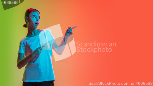 Image of Young caucasian girl\'s portrait on gradient green-orange studio background in neon light