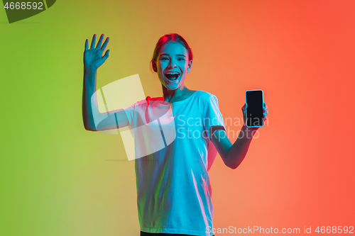 Image of Young caucasian girl\'s portrait on gradient green-orange studio background in neon light