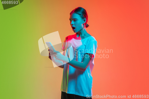 Image of Young caucasian girl\'s portrait on gradient green-orange studio background in neon light