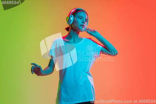 Image of Young caucasian girl\'s portrait on gradient green-orange studio background in neon light