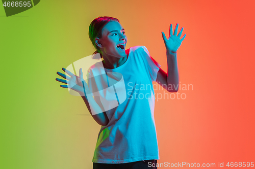 Image of Young caucasian girl\'s portrait on gradient green-orange studio background in neon light