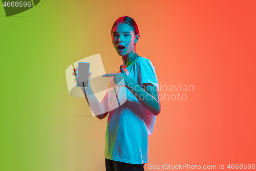 Image of Young caucasian girl\'s portrait on gradient green-orange studio background in neon light