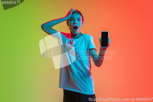 Image of Young caucasian girl\'s portrait on gradient green-orange studio background in neon light