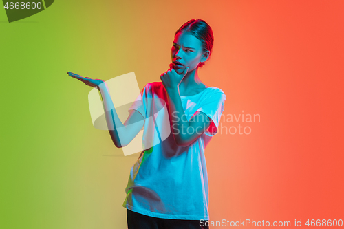 Image of Young caucasian girl\'s portrait on gradient green-orange studio background in neon light