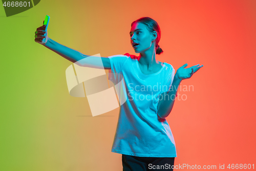 Image of Young caucasian girl\'s portrait on gradient green-orange studio background in neon light